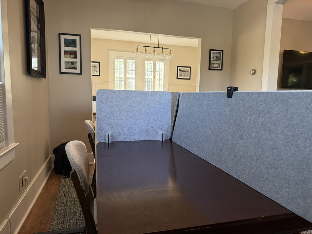 Two partitioned carrel desks with grey fabric dividers along the wall at Eiswork, framed ski photographs above